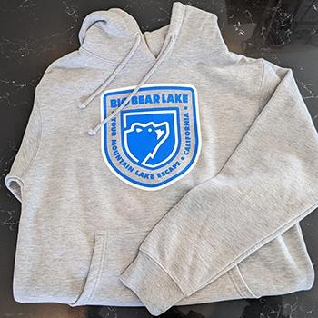 A light gray T-shirt with the Big Bear Lake Visitor Center Logo being displayed, the shirt is on a counter.