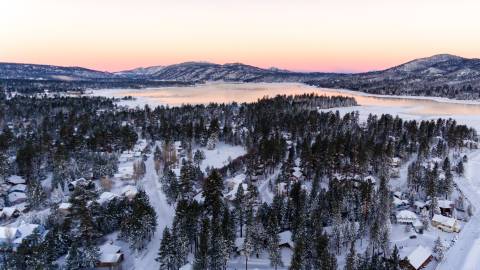 An overhead photo of a winter snowfall in Big Bear Lake, the sunset pink-ish orange sunset reflecting on the lake.