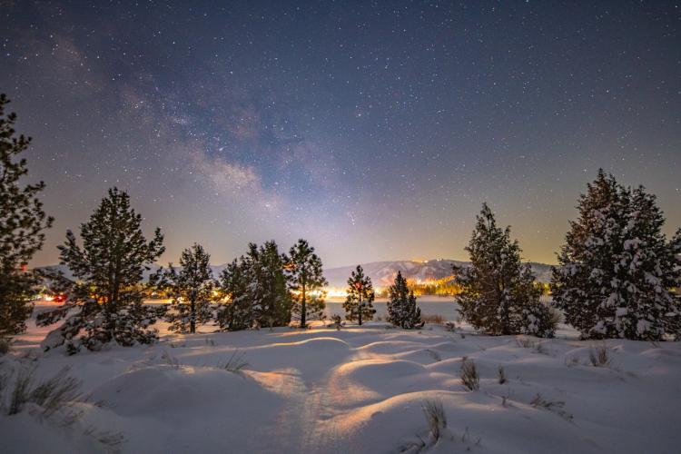 A photo of Big Bear's night sky taken during winter after a snowfall, the bright stars and a galaxy are visible.
