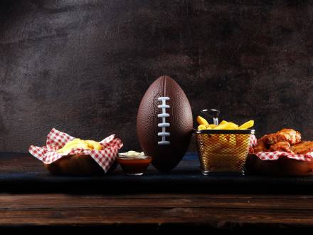 A football sits on a wooden table with appetizers including french fries and chicken wings. Stock image.