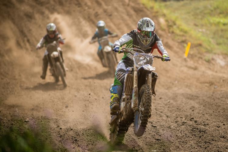 Three BMX bikers competing in a race on a BMX track with one of the riders in the front pulling off a wheelie.