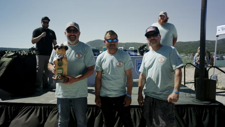 A photo of the 1st, 2nd, and 3rd place 2025 FF50K men winners, the first place winner is holding a 1st place bear trophy.