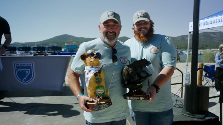 A photograph of the 1st 2025 FF50K winner, the first place winner is holding a 1st place bear trophy and largest catch trophy