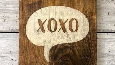 एक लकड़ी का चिन्ह जिस पर XOXO लिखा है, सफेद पृष्ठभूमि पर रखा है।