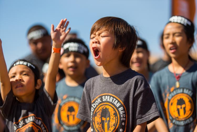 A crowd of young kids wearing Spartan Race shirts cheer on competitors at the Spartan Trifecta Weekend in Big Bear Lake, CA.