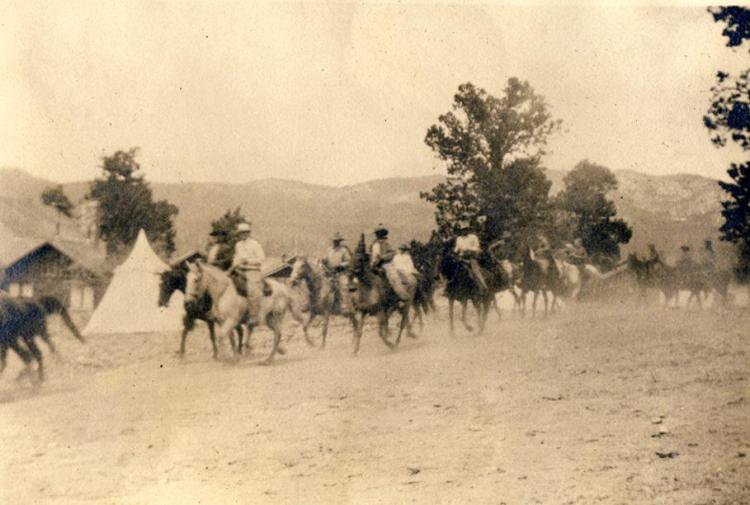 An old photo of a group of men on horses in Big Bear Valley, behind them houses and tents are visible.